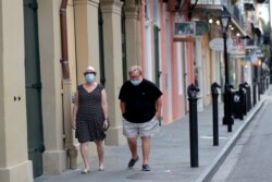 FILE - A couple walks past shuttered businesses impacted by the coronavirus epidemic, on Royal St, in the French Quarter of New Orleans, May 12, 2020.