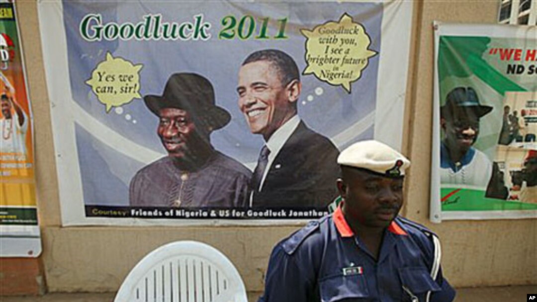 A Nigerian security man sits under a campaign poster of Nigeria President Goodluck Jonathan, with US President Barrack Obama, in Abuja, Nigeria, January 12, 2011