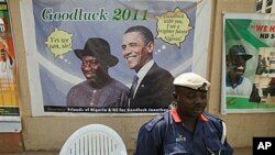 A Nigerian security man sits under a campaign poster of Nigeria President Goodluck Jonathan, with US President Barrack Obama, in Abuja, Nigeria, January 12, 2011