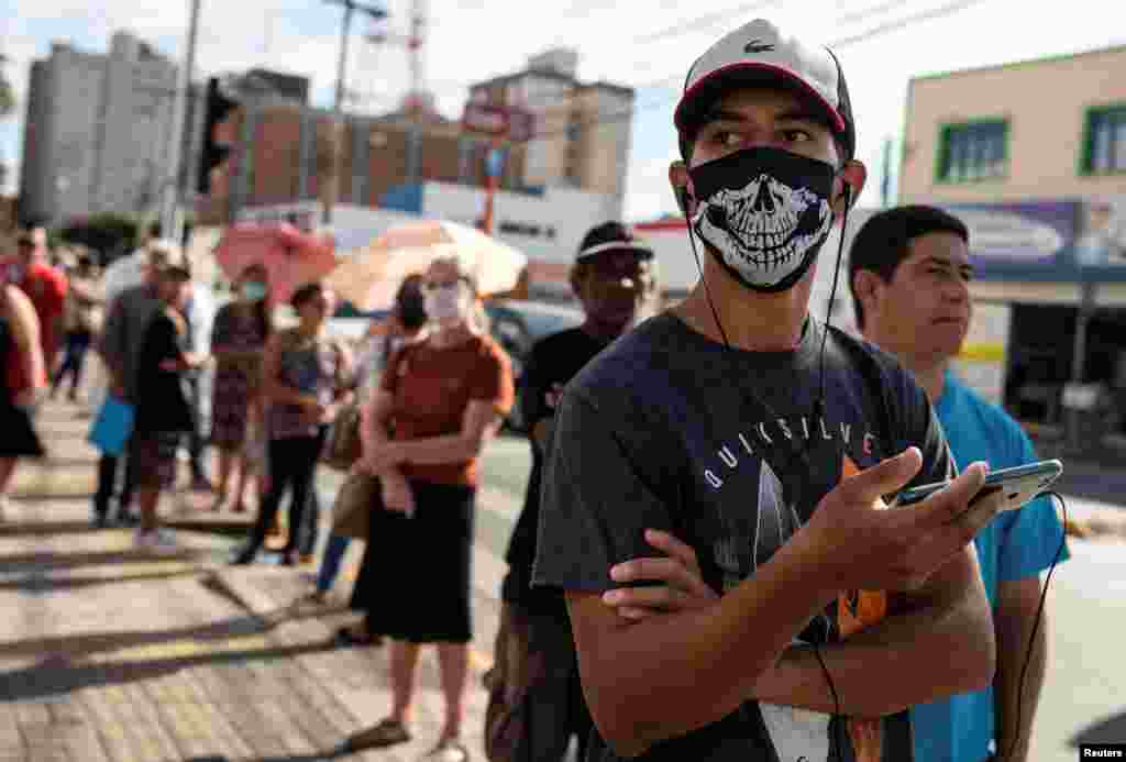 Brasil: Personas esperan en fila frente a un banco público para tratar de recibir ayuda de emergencia dada por el gobierno federal a los más vulnerables, en medio del brote de la enfermedad por coronavirus en Jacarei, estado de Sao Paulo. Todos guardan el distanciamiento social estipulado y usan mascarillas.