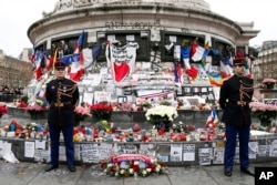 French honor guards stand next to the monument at Place de la Republique in Paris, where people laid candles cards and flags during a ceremony to honor the victims of the Islamic extremist attacks, Jan. 10, 2016.