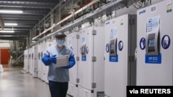 FILE - A worker passes a line of freezers holding coronavirus disease (COVID-19) vaccine candidate BNT162b2 at a Pfizer facility in Puurs, Belgium in an undated photograph. 