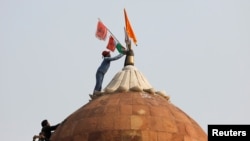 A man holds a flag as he stands on the top of the historic Red Fort during a protest against farm laws introduced by the government, in Delhi, India, Jan. 26, 2021. 