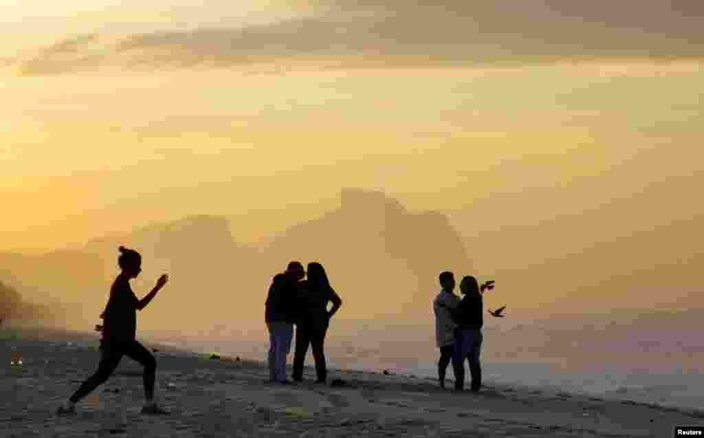 People are pictured during sunrise on a beach at the Parque Natural Municipal de Marapendi natural reserve near the Olympic park for the Rio 2016 Summer Olympic Games in Rio de Janeiro, Brazil.