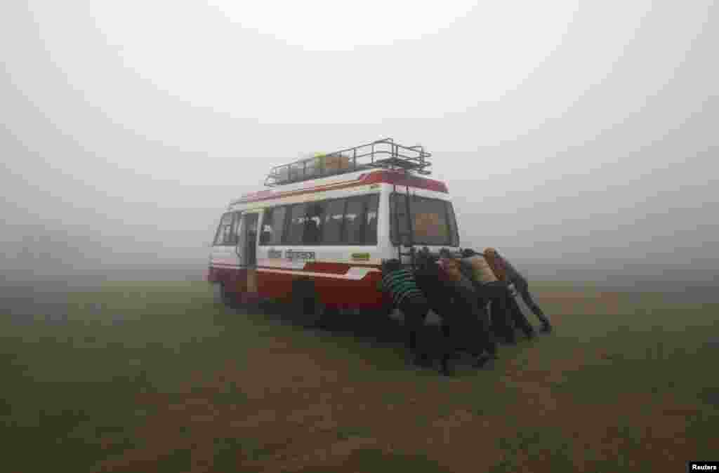 Para penumpang membantu mendorong bus yang mogok, pada suatu pagi yang dingin dan berkabut di kota Agartala, negara bagian Tripura, India. 