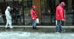 Employees of the local cleaning company 'Deratizer' wearing face masks with filters disinfect a street as snow falls in Sarajevo, March 24, 2020