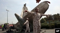 အီရန်တော်လှန်ရေးအစောင့်တပ်ဖွဲ့ဝင်တွေက လေယာဉ်ပျက်နားကပ်လာတဲ့ သတင်းထောက်တွေကို တားမြစ်နေစဉ်။ (သြဂုတ် ၁၀၊ ၂၀၁၄)