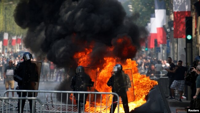Un inodoro portátil se quema junto a los gendarmes franceses durante los enfrentamientos con manifestantes en la avenida de los Campos Elíseos, en París, Francia, el 14 de julio de 2019. REUTERS.