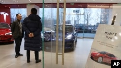 A sales staff chats with a customer at a Tesla store near a poster announcing orders of the Model 3 electric cars in Beijing, China, Monday, Jan. 7, 2019. 