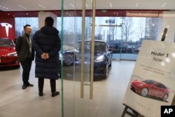 A sales staff chats with a customer at a Tesla store near a poster announcing orders of the Model 3 electric cars in Beijing, China, Monday, Jan. 7, 2019.