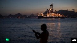 FILE - A man holds his fishing rod, carrying an illuminated bobber, on the shore of Guanabara Bay where Petrobras operates its ultra-deep drilling vessel Laguna Star NS-44, in Niteroi, Brazil.
