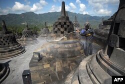 Seorang pekerja membersihkan abu vulkanik dari stupa di Candi Borobudur di Kabupaten Magelang pada 22 Juni 2020, sehari setelah Gunung Merapi meletus di dekat Sleman. (Foto: AFP)