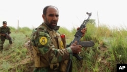 FILE - Iraqi Shiite Hezbollah Brigade militiamen take combat positions in the front line against the Islamic State group in Khalidiya, 100 kilometers (60 miles) west of Baghdad, Iraq.