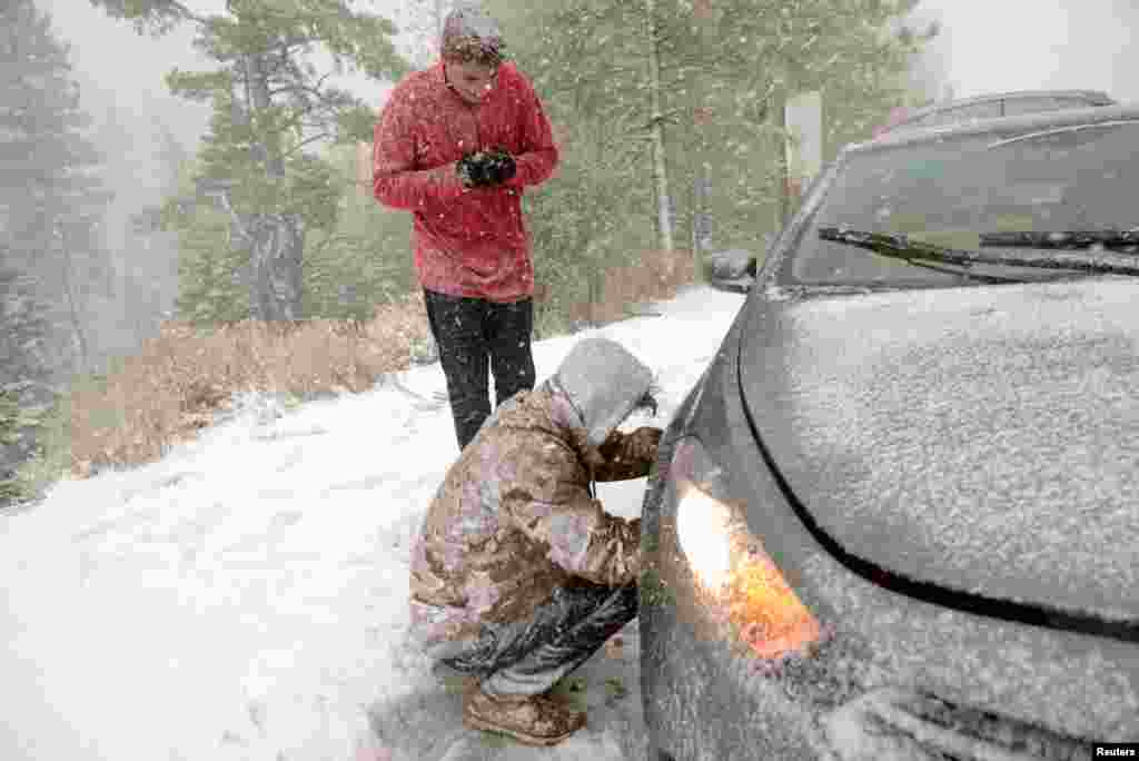 Jacob Ackman of Reno, Nevada, warms his hands as his friend Tiger Bortin installs chains on the wheels of their vehicle, on the side of Highway 88 in Woodford, California, Nov. 24, 2015, as a winter storm hits the drought-stricken state.