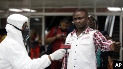 Un agent de la santé portuaire utilise un thermomètre sur un travailleur dans le hall d'arrivée de l'aéroport international Murtala Muhammed de Lagos, au Nigeria, le mercredi 6 août 2014. (AP Photo/Sunday Alamba)