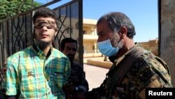 FILE - Members of the Syrian Democratic Forces escort a blindfolded civilian detainee suspected of being an Islamic State militant in Raqqa, Syria, Oct. 12, 2017. 