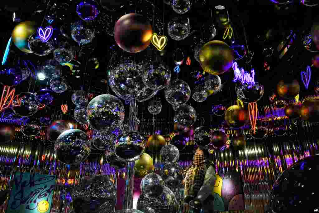 A woman looks at the disco and Christmas balls illuminated with lights hanging for the upcoming Christmas Festival at a popular outdoor shopping mall in Beijing, China.