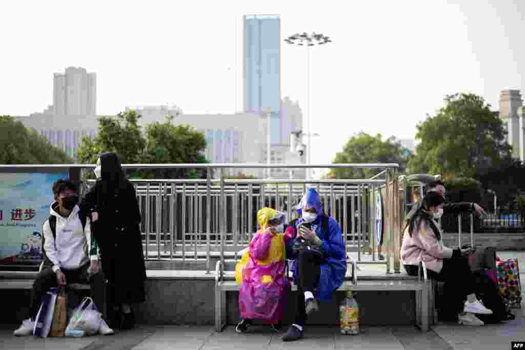 Las personas con máscaras faciales se sientan frente a la estación de tren de Hankou en Wuhan, a donde llegan con la esperanza de tomar uno de los primeros trenes que salen de la ciudad en la provincia central de Hubei de China.