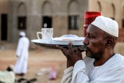 Seorang pria membawa nampan makanan dan air minum untuk diberikan kepada tamu yang ikut berbuka puasa Ramadhan di desa al-Nuba, sekitar 50 kilometer selatan ibu kota Sudan, 22 April 2021. (AFP)