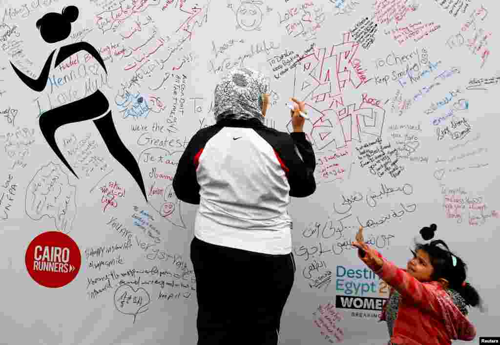 A woman whose daughter stands next to her writes a message of support during the first Egyptian women&#39;s race. The cause aims to raise awareness about violence against women, in Cairo, Egypt.