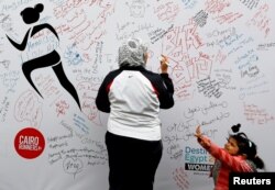 FILE - A woman, with her daughter, writes a message of support during the first Egyptian womens' race, to raise awareness about violence against women, in Cairo, Egypt, Nov. 30, 2018.
