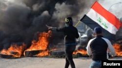 A demonstrator holds an Iraqi flag near burning tires during ongoing anti-government protests in Nassiriya, Iraq, Nov. 24, 2019.