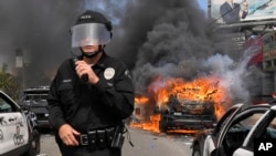Los Angeles Police Department commander Cory Palka stands among several destroyed police cars as one explodes while on fire during a protest over the death of George Floyd, May 30, 2020, in Los Angeles. 