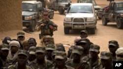 FILE - A French soldier stands watch behind Malian soldiers during a visit by the head of France's Operation Serval and Mali's army chief of staff to a Malian army base in Kidal, Mali. 