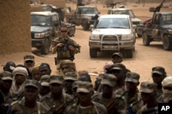 FILE - A French soldier stands watch behind Malian soldiers during a visit by the head of France's Operation Serval and Mali's army chief of staff to a Malian army base in Kidal, Mali.