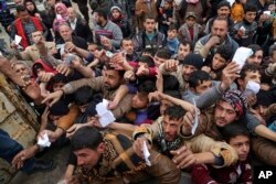 FILE - Civilians present their rations cards in order to receive humanitarian food aid, in the eastern side of Mosul, Iraq, Jan. 31, 2017.