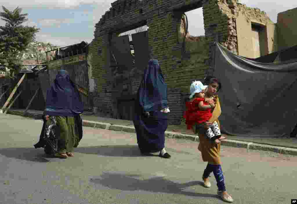 Afghan women in burqas and children walk on a street in Kabul, Afghanistan.