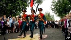 FILE - Schoolchildren watch as servicemen carry a flag of the Russia-backed self-proclaimed separatist Donetsk republic, at a ceremony on the first day of school in Donetsk, Ukraine, Sept. 1, 2017. Ukrainian government and pro-Russia separatists in eastern Ukraine have recently agreed to a cease-fire to help reduce tensions as the new school year starts.