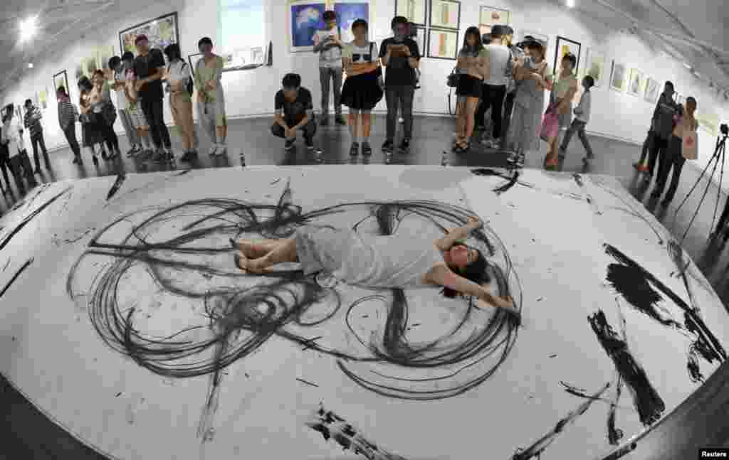 An art student lies on a giant canvas as she paints with her limbs at an exhibitionof the faculty of the Hubei Institute of Fine Arts, in Wuhan, Hubei province, China.