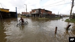 A boy pushes his bicycle in a flooded street after heavy rains at Jardim Pantanal neighborhood in Sao Paulo, 15 Jan 2011