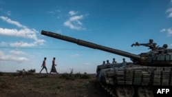 Tampak dua orang remaja berjalan di sebelah tank yang sudah tidak terpakai milik pasukan pemberontak Tigray di Mehoni, Ethiopia, pada 11 Desember 2020. (Foto: AFP/Eduardo Soteras)