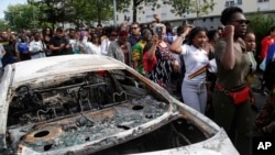 People walk past a charred car during a march after police shot a driver apparently trying to avoid an identity check earlier this week, July 5, 2018 in Nantes, western France.