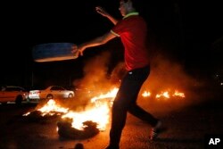FILE - A man burns tires during a protest demanding services and jobs in Basra, 340 miles (550 kilometers) southeast of Baghdad, Iraq, July 13, 2018.