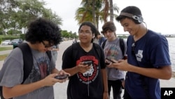 FILE -- Brian Vega, left, Peyton Ruiz, second from left, and Max Marrero, right, check their smartphones at Bayfront Park in downtown Miami, Florida.