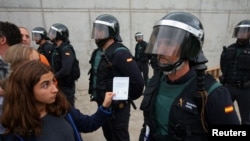 A woman shows a ballot to a Spanish Civil Guard officer outside a polling station for the banned independence referendum in Sant Julia de Ramis, Spain, Oct. 1, 2017. 