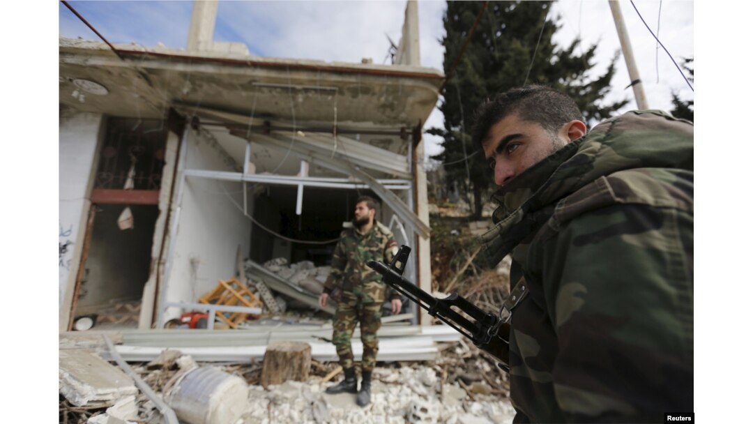 Forces loyal to Syria's President Bashar al-Assad stand in front of damaged shops in the town of Rabiya after they recaptured the rebel-held town in coastal Latakia province, Syria, Jan. 27, 2016.