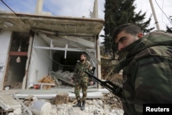 Forces loyal to Syria's President Bashar al-Assad stand in front of damaged shops in the town of Rabiya after they recaptured the rebel-held town in coastal Latakia province, Syria, Jan. 27, 2016.