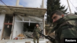 FILE - Forces loyal to Syria's President Bashar al-Assad stand in front of damaged shops in the town of Rabiya after they recaptured the rebel-held town in coastal Latakia province, Syria, Jan. 27, 2016. 