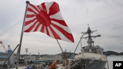 FILE - Japan's military flag, the rising sun flag, flutters on the Japan Maritime Self-Defense Force tank landing ship JS Kunisaki anchored in Yokosuka near Tokyo, May 27, 2014.