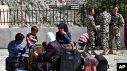 Displaced people who fled the Syrian war sit on their belongings near the Lebanese-Syrian border as they prepare to return to their village of Beit Jinn in Syria, while Lebanese General Security soldiers stand guard, in the southern village of Shebaa, Lebanon, Wednesday, April, 18, 2018.