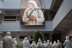 FILE - Nuns from the Missionaries of Charity attend a special prayer to mark the 111th birth anniversary of Mother Teresa near a banner with her picture at the Mother House in Kolkata, Aug. 26, 2021.