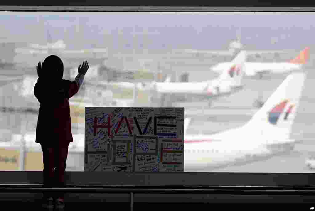 Uma menina observa os aviões da janela da sala de espera do Aeroporto Internacional de Kuala Lumpur em Sepang. Ao lado dela está um cartaz que diz: Tenham Esperança. Malásia, Março 10, 2014.