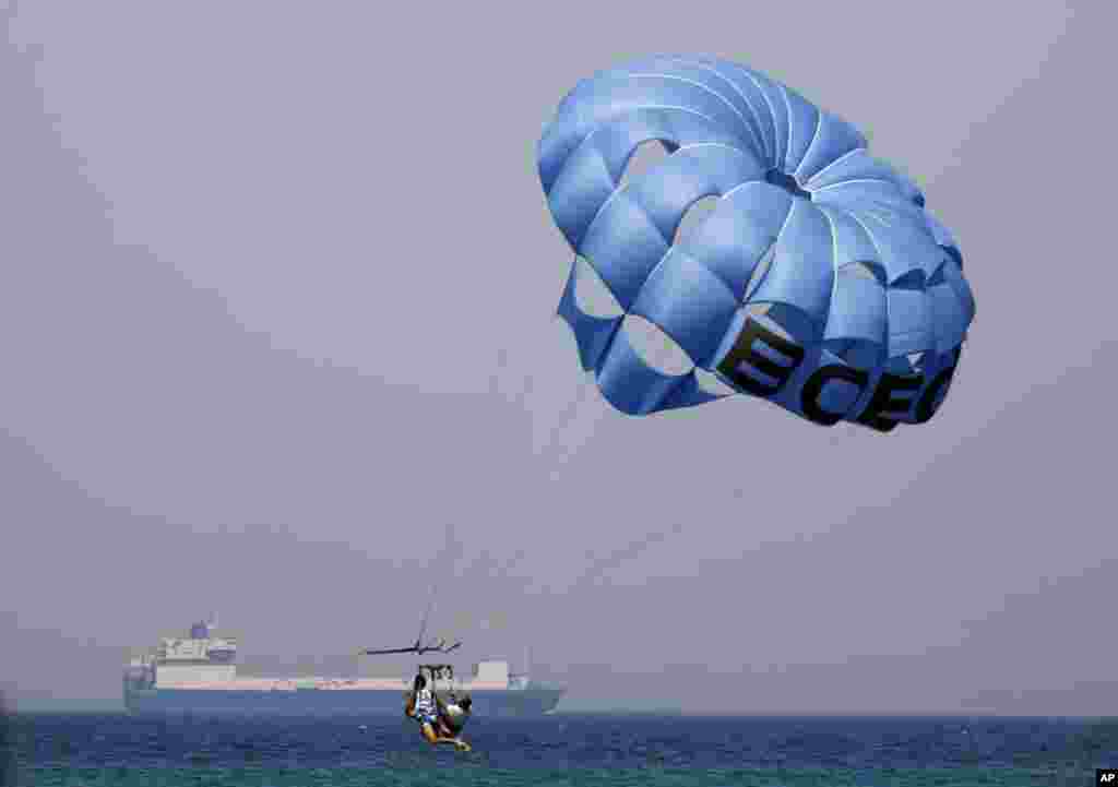 Vacationers parasail as a cargo ship passes behind them on the Gulf of Suez toward the Red Sea, at El Sokhna beach in Suez, Egypt.