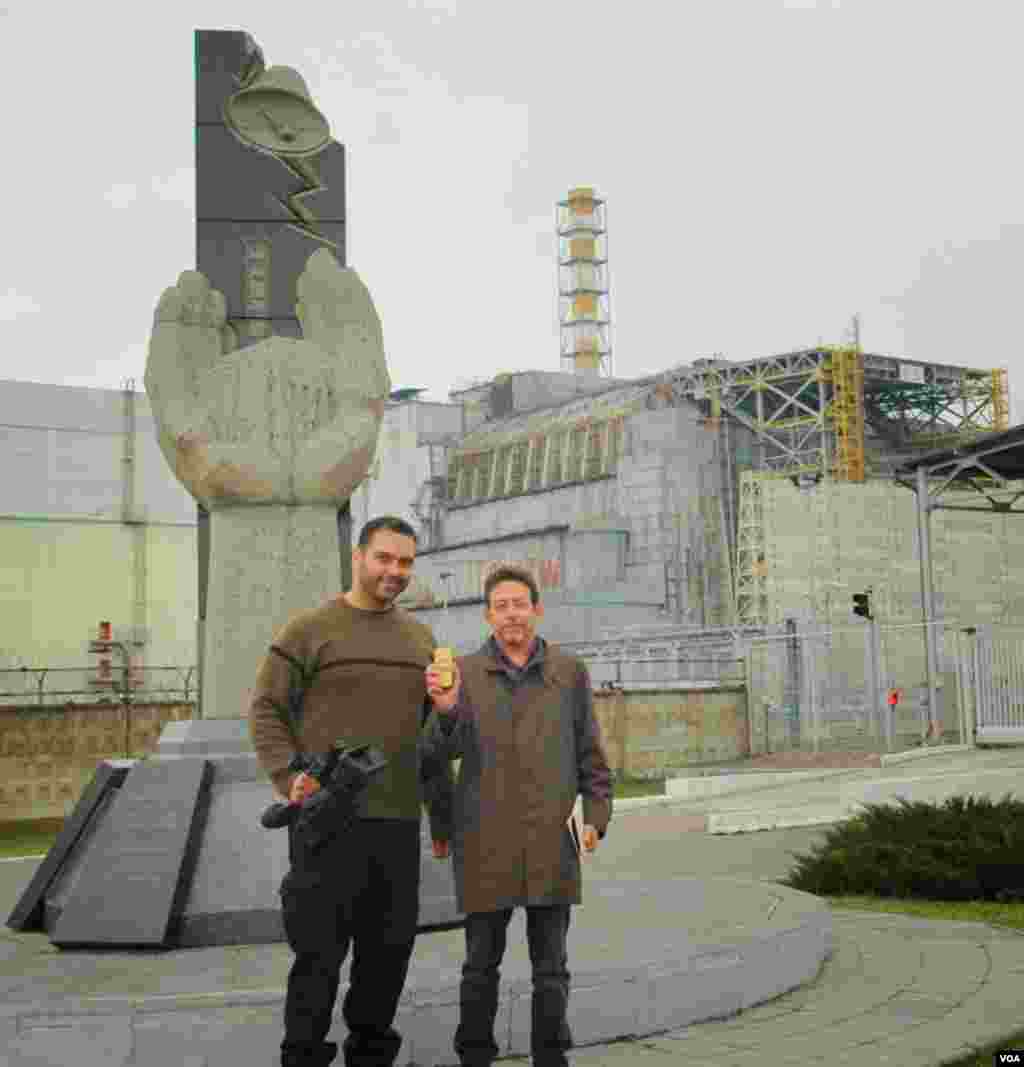 Os correspondentes da VOA Arash Arabasadi e Steve Herman (segurando um monitor de radiação) em frente do antigo sarcófago que cobre o Reactor No. 4 de Chernobyl Reactor No. 4, Fábrica de Energia Nuclear de Chernobyl, Ucrânia, Março 19, 2014. (unknown photographer/VOA)