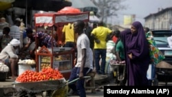 DOSSIER - Dans cette photo d'archive du 24 décembre 2020, des gens marchent dans un marché à Lagos, au Nigéria.  Près de 20% des 4 500 personnes interrogées dans l'étude sur les jeunes dans 15 pays africains ont déclaré qu'elles étaient devenues sans emploi à cause de la pandémie.  Certains d'entre eux se tournent vers la vente de produits agricoles ou d'autres biens dans la rue.  (AP Photo/Dimanche Alamba, Dossier)