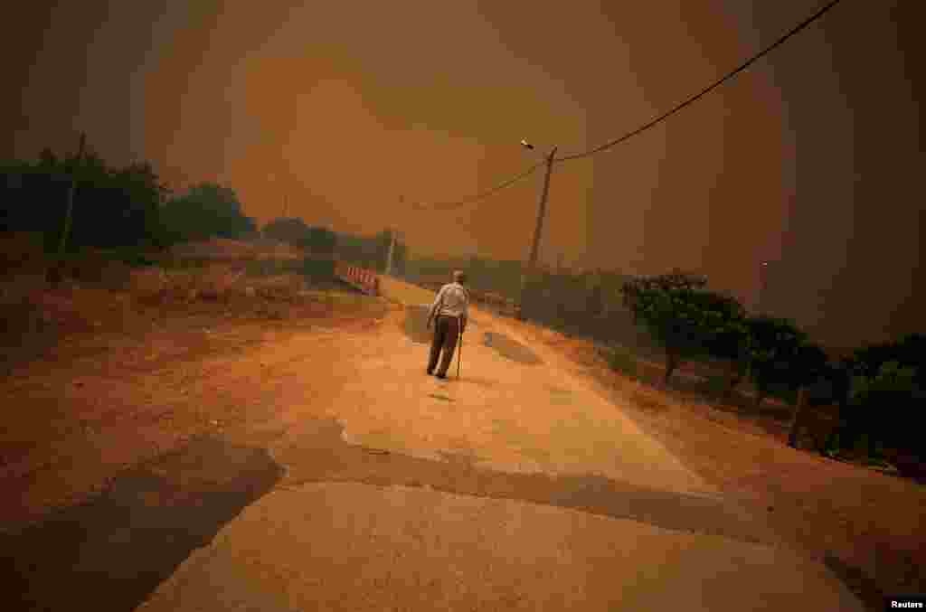 A man walks on a road as fire approaches Pedreira, near Silves, Portugal.